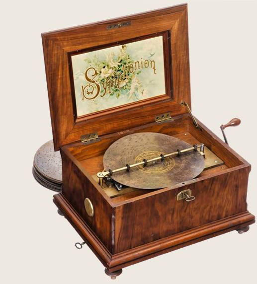 Caja de música Symphonion abierta, con litografía dorada en la tapa, disco metálico en el plato y una pila de discos al lado